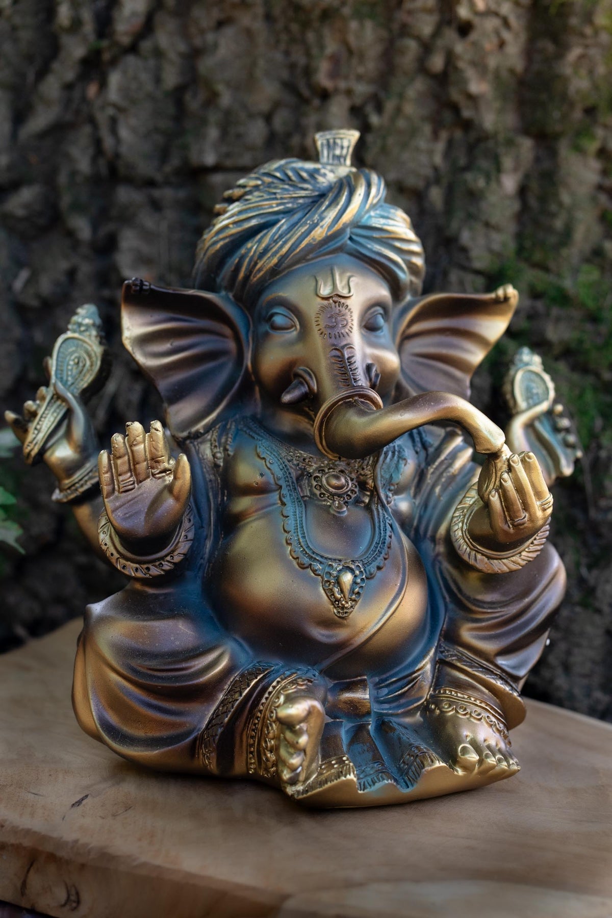 Figura de Ganesha sentada con turbante, tonos dorados y oscuros y matices azulados