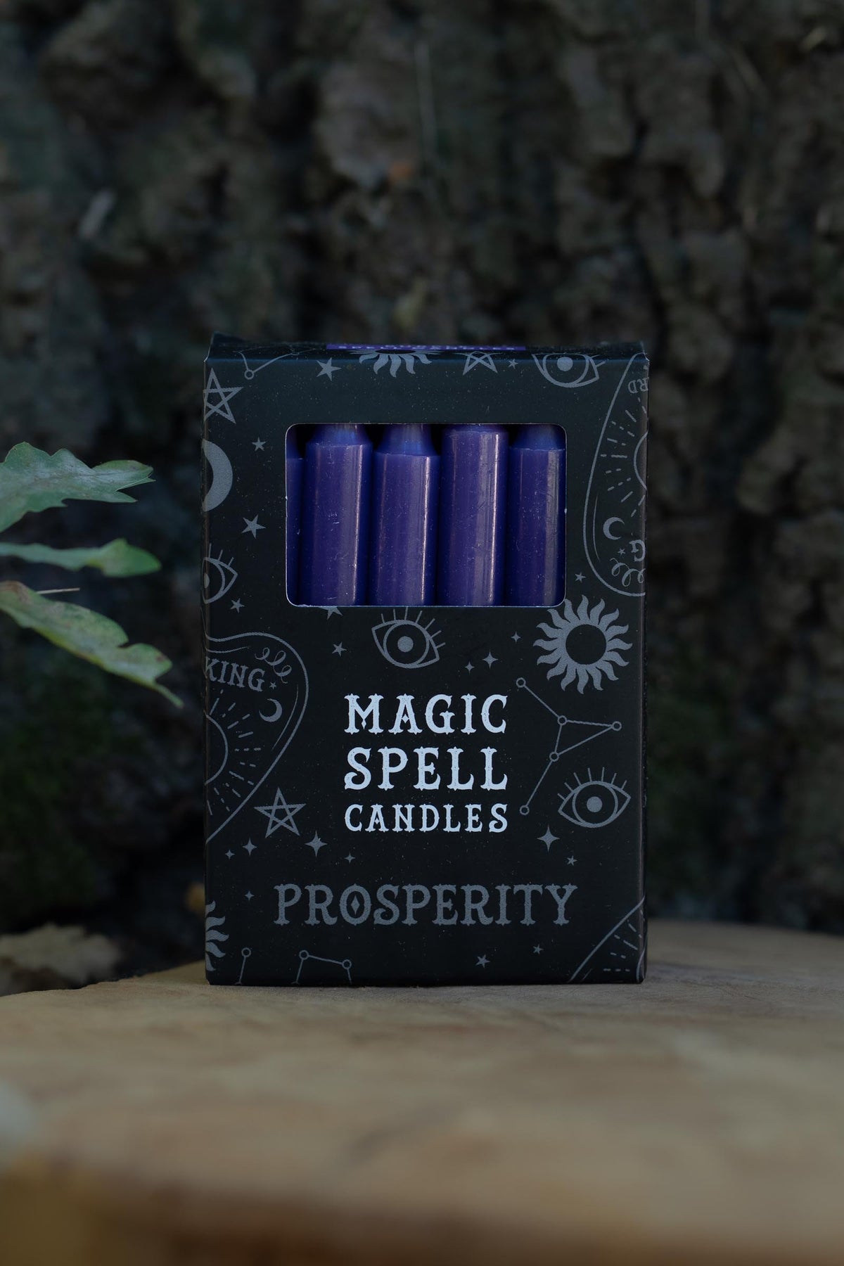 Caja negra Magic Spell Candles Prosperity con velas moradas y símbolos celestes.