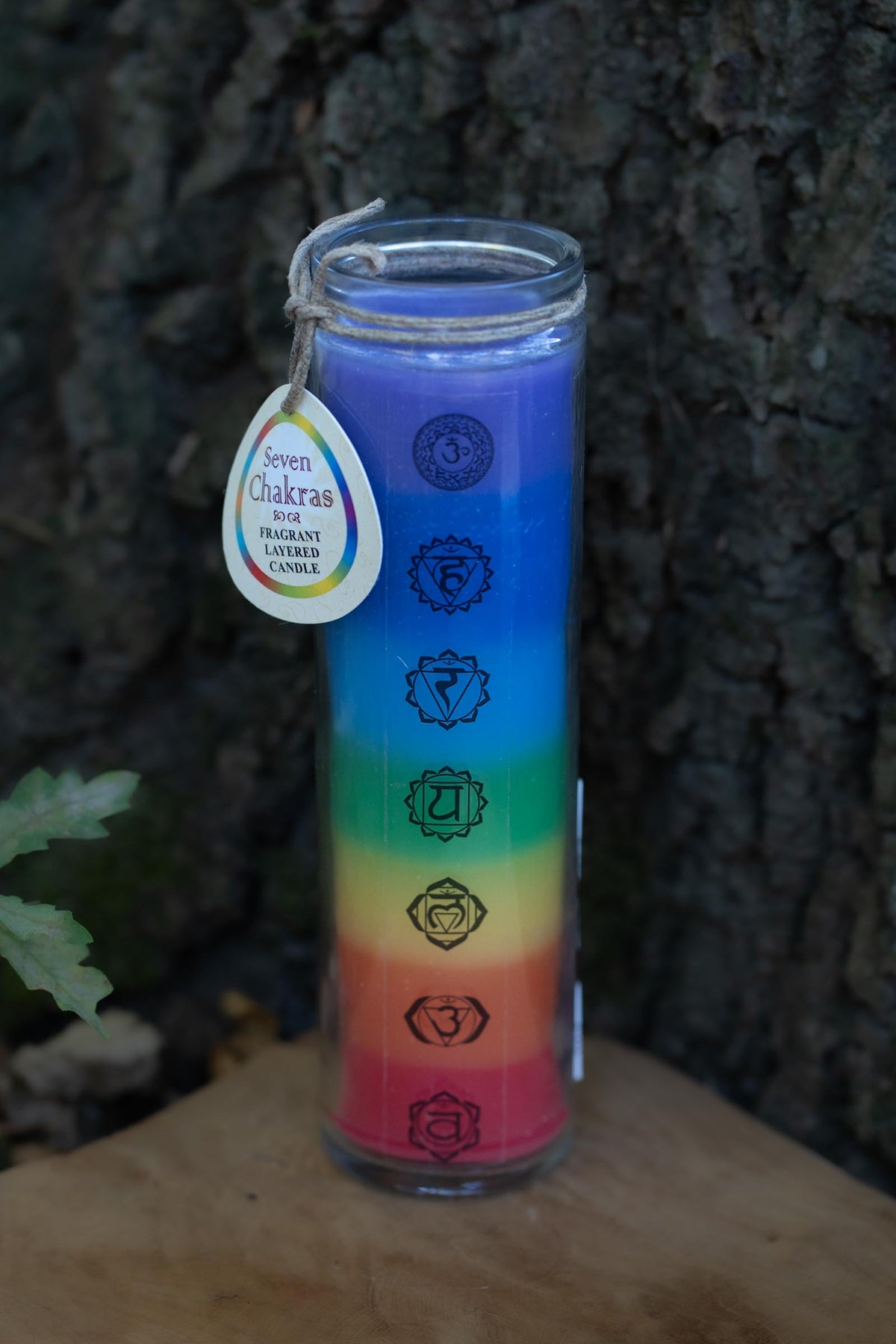 Vela aromática de siete capas de colores en recipiente transparente con los símbolos de los siete chakras.