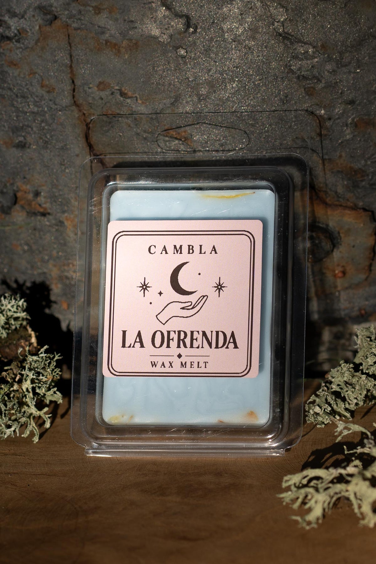 La Ofrenda Wax Melt de Cambla en packaging transparente azul celeste sobre madera con musgo